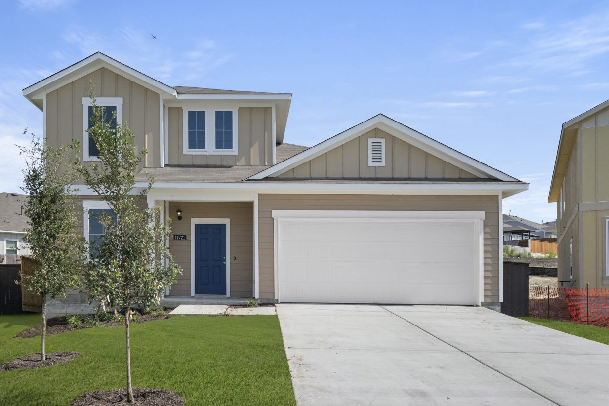 Front exterior of a tan two-story home with a blue front door, white garage, and green landscape.