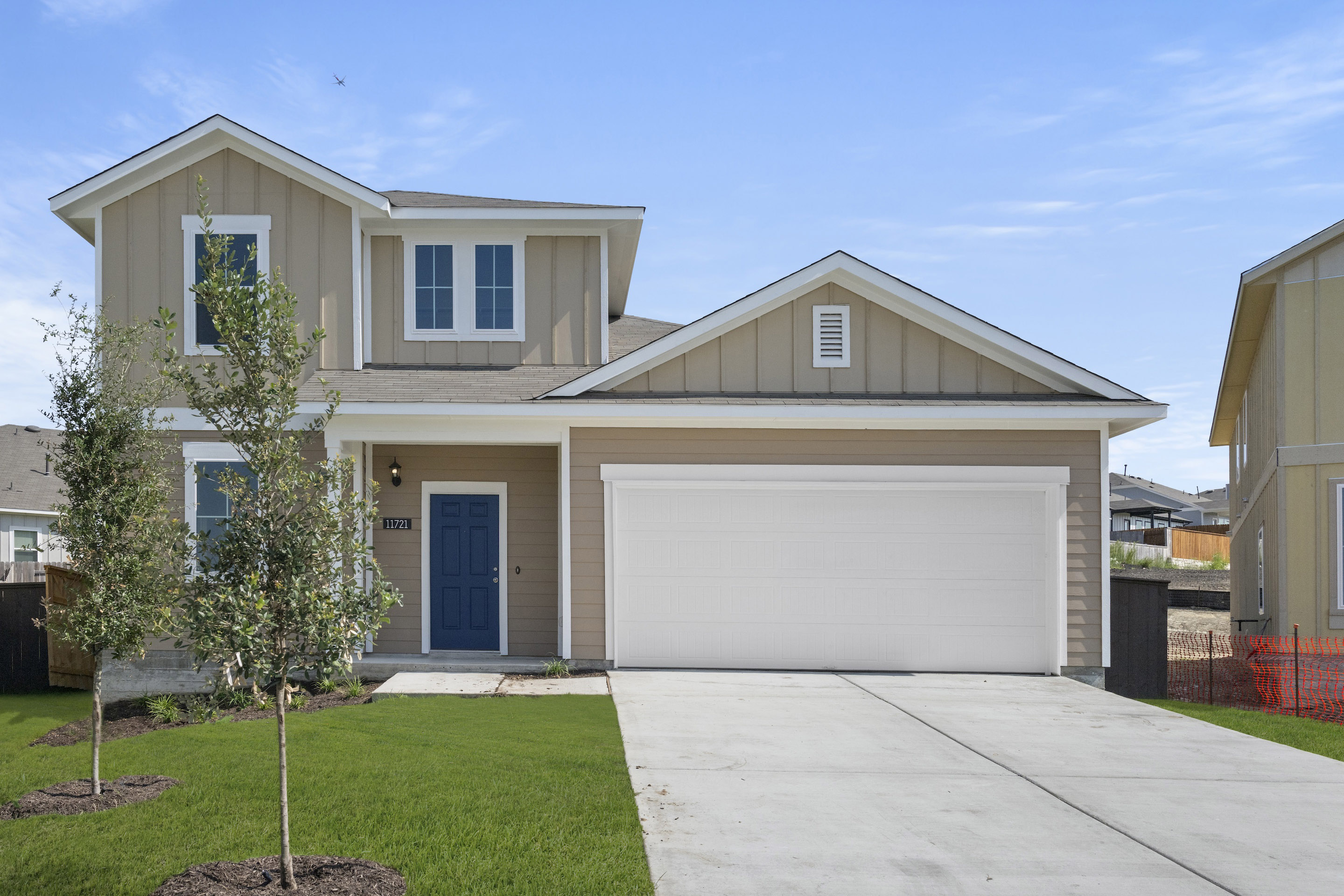 Front exterior of a tan two-story home with a blue front door, white garage, and green landscape.