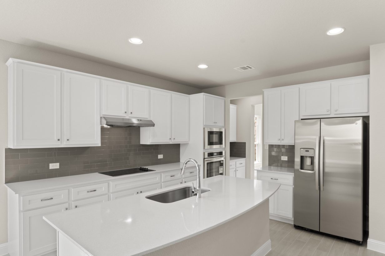A Kitchen with white countertops, white cabinets, steel appliances, and gray blacksplash tile, white painted walls and vinyl flooring.