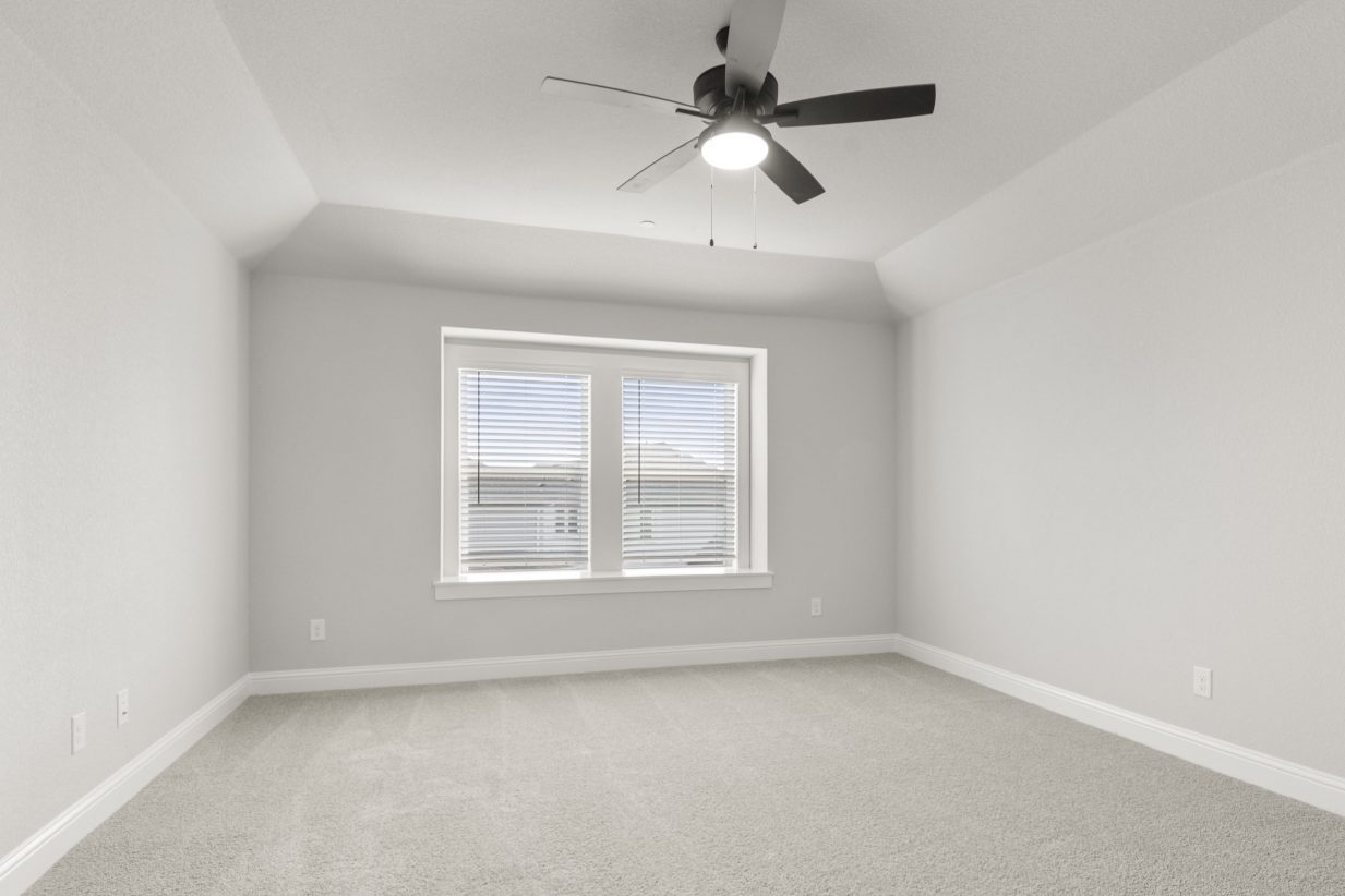 The primary bedroom with tan carpet, white walls, white framed windows, and a black ceiling fan.