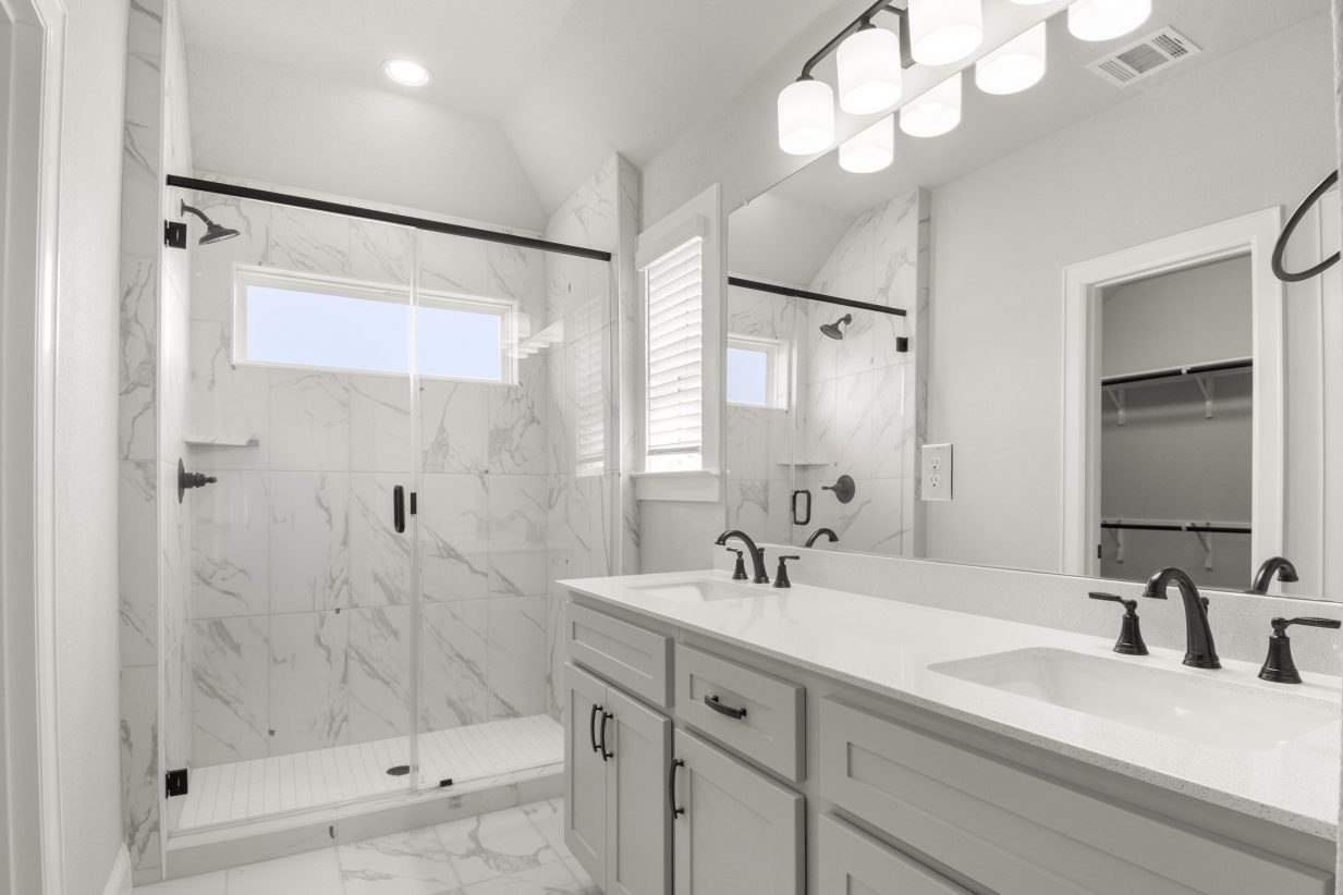 Interior image of a bathroom with dual vanity with grey cabinets and white countertops, and a walk-in shower.