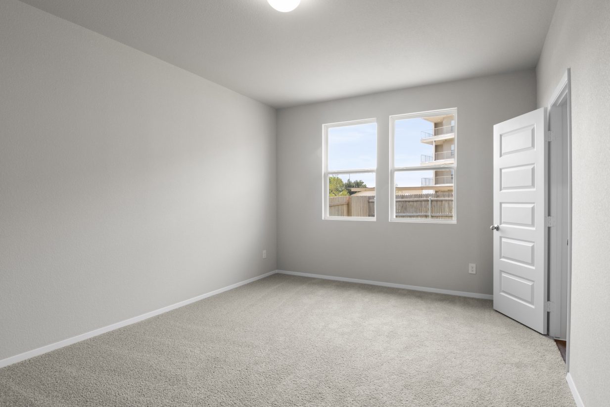 Interior image of a bedroom with white walls, windows, ceiling light and tan carpeting.