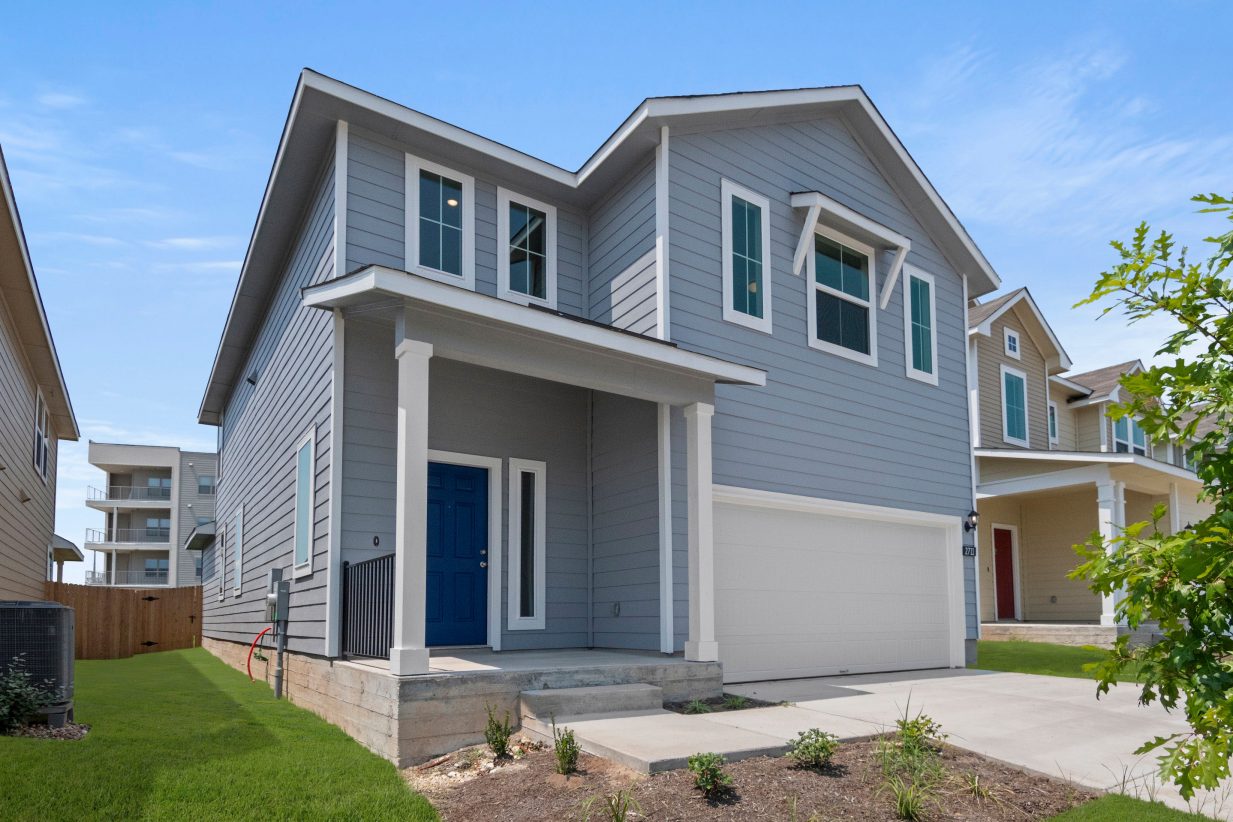 Exterior of a two-story blue home with a green landscape with trees.
