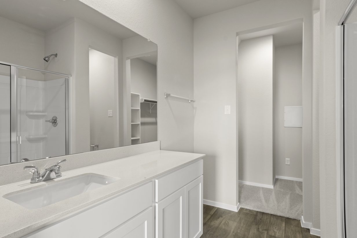 Image of bathroom with white vanity and cabinets. Reflection of shower in mirror and doorway to walk-in closet