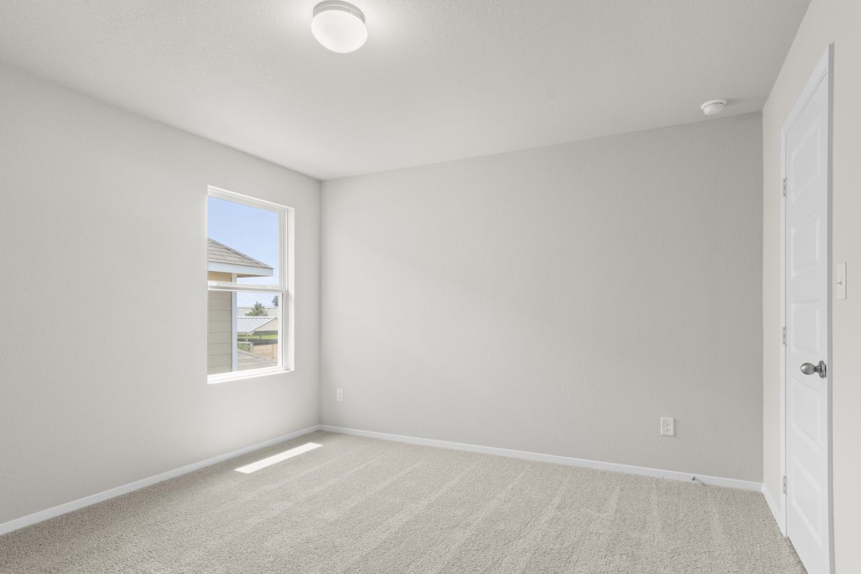 Interior image of a bedroom with white walls, a window, ceiling light and tan carpeting.
