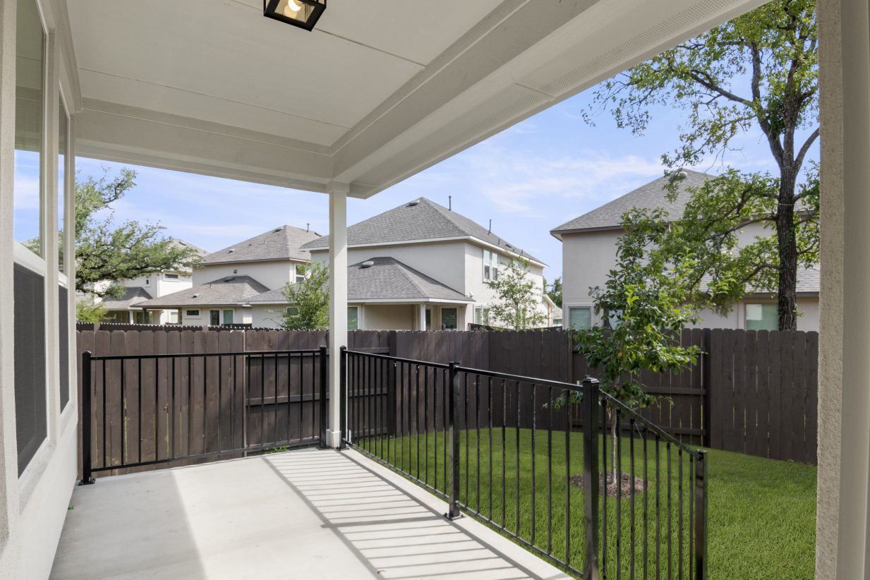 The back concrete patio with black fencing and green landscape.