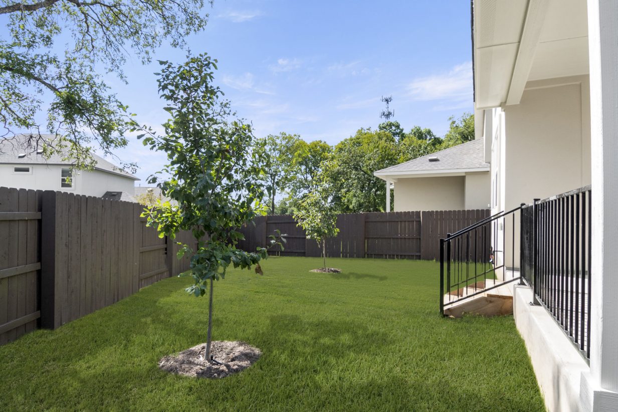Exterior of the back of the two-story home with green landscape and brown fence.