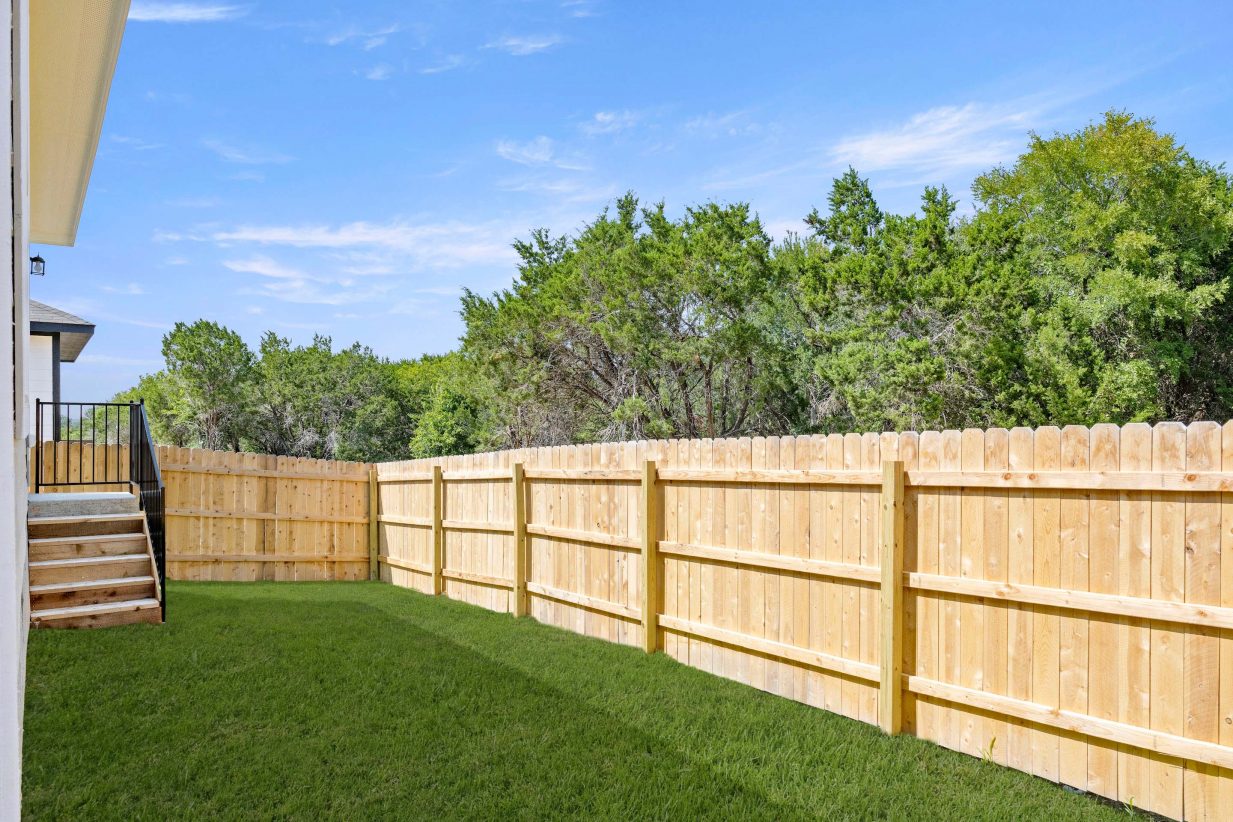 Backyard with stairs, green grass, and a tan fence.