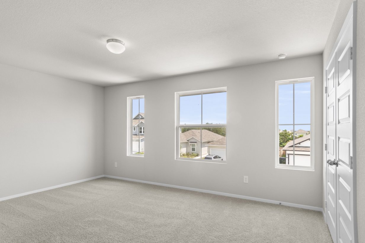 Interior image of a bedroom with white walls, windows and tan carpeting.
