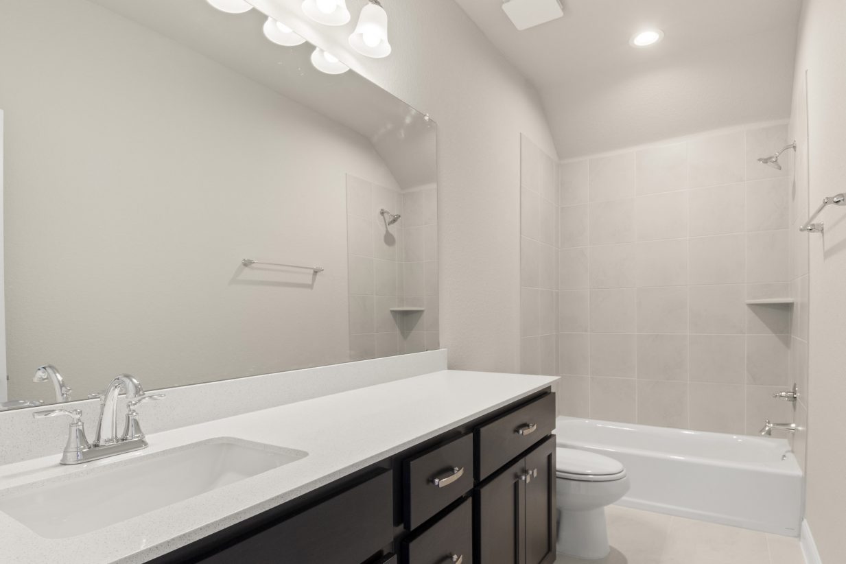A bathroom with white countertops, brown cabinets, a mirror, and white bathtub and toilet.