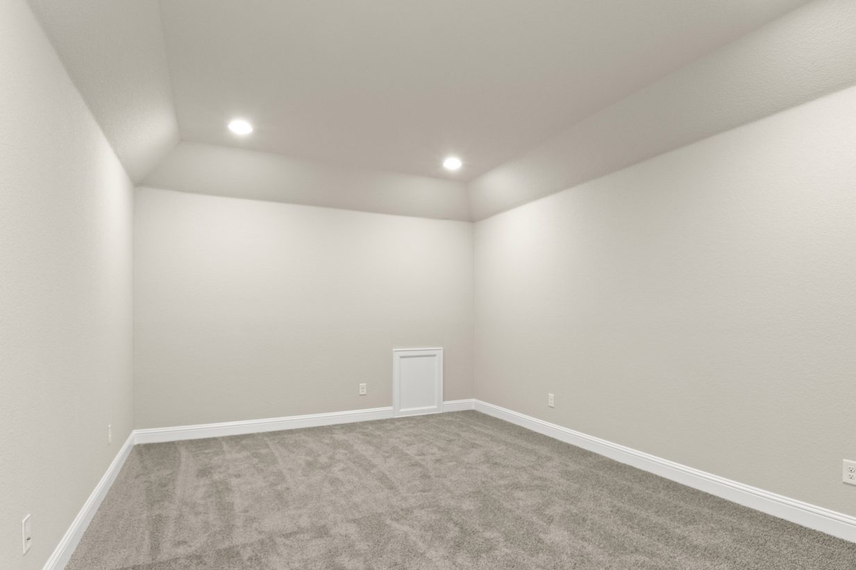 Media room with tan carpet, cream painted walls and white base boards.