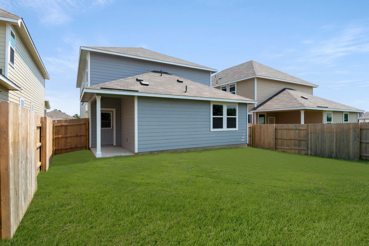 Exterior of a two-story blue home with a fenced backyard with green grass.