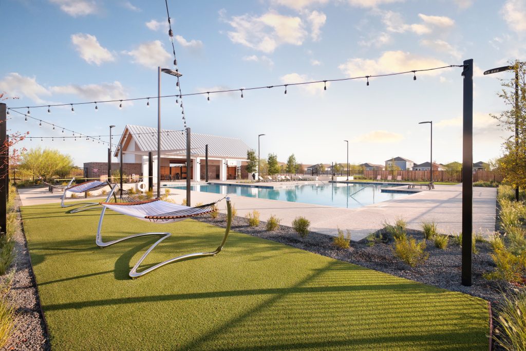 Photo of amenity center in Brohn Homes Hymeadow in Maxwell, TX. Free-standing hammocks in grass with string lights above. Pool and building in background.