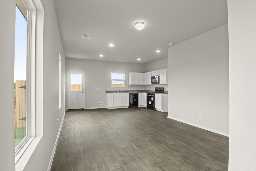 Image of home interior with wood-look floor, windows, and kitchen in rear