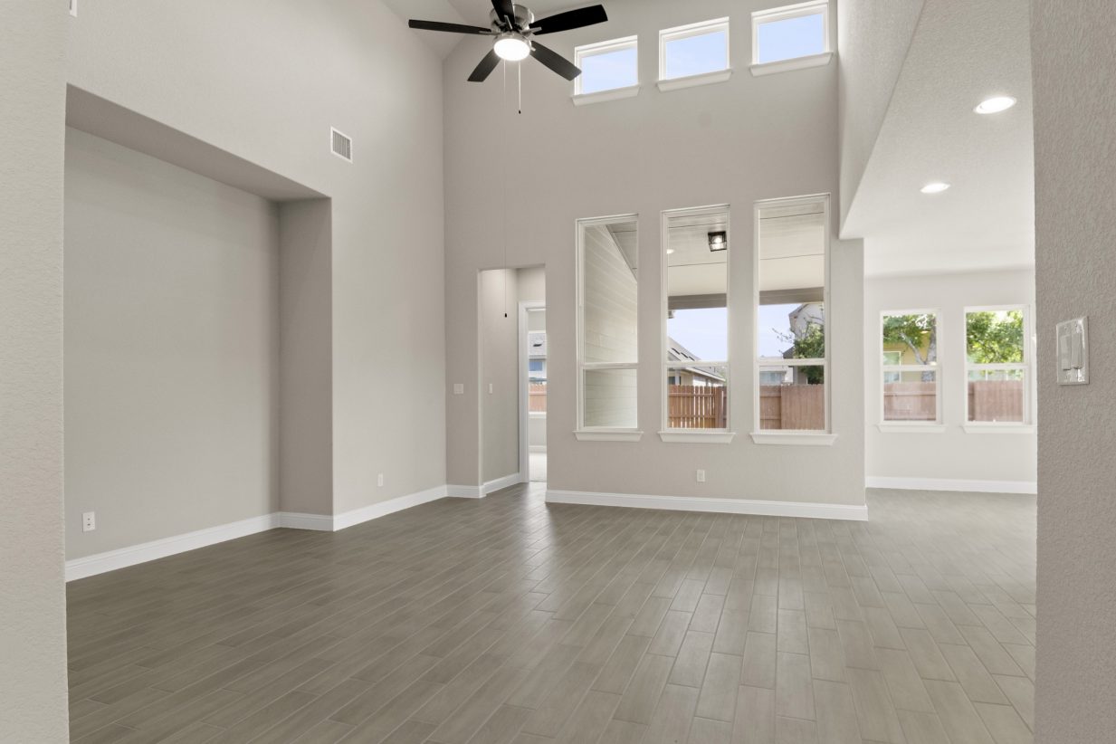 A living room room with vinyl flooring, white-framed windows, and white painted walls.