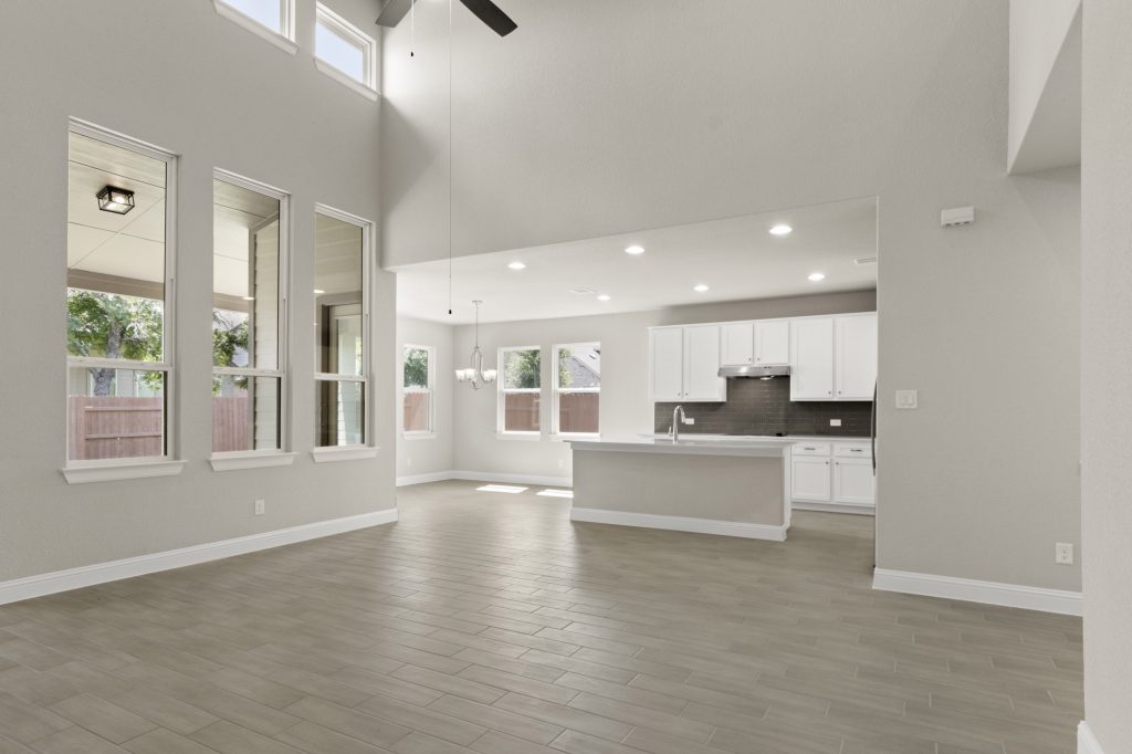 Kitchen and living room with white countertops, white cabinets, steel appliances, and gray blacksplash tile, white painted walls and vinyl flooring.