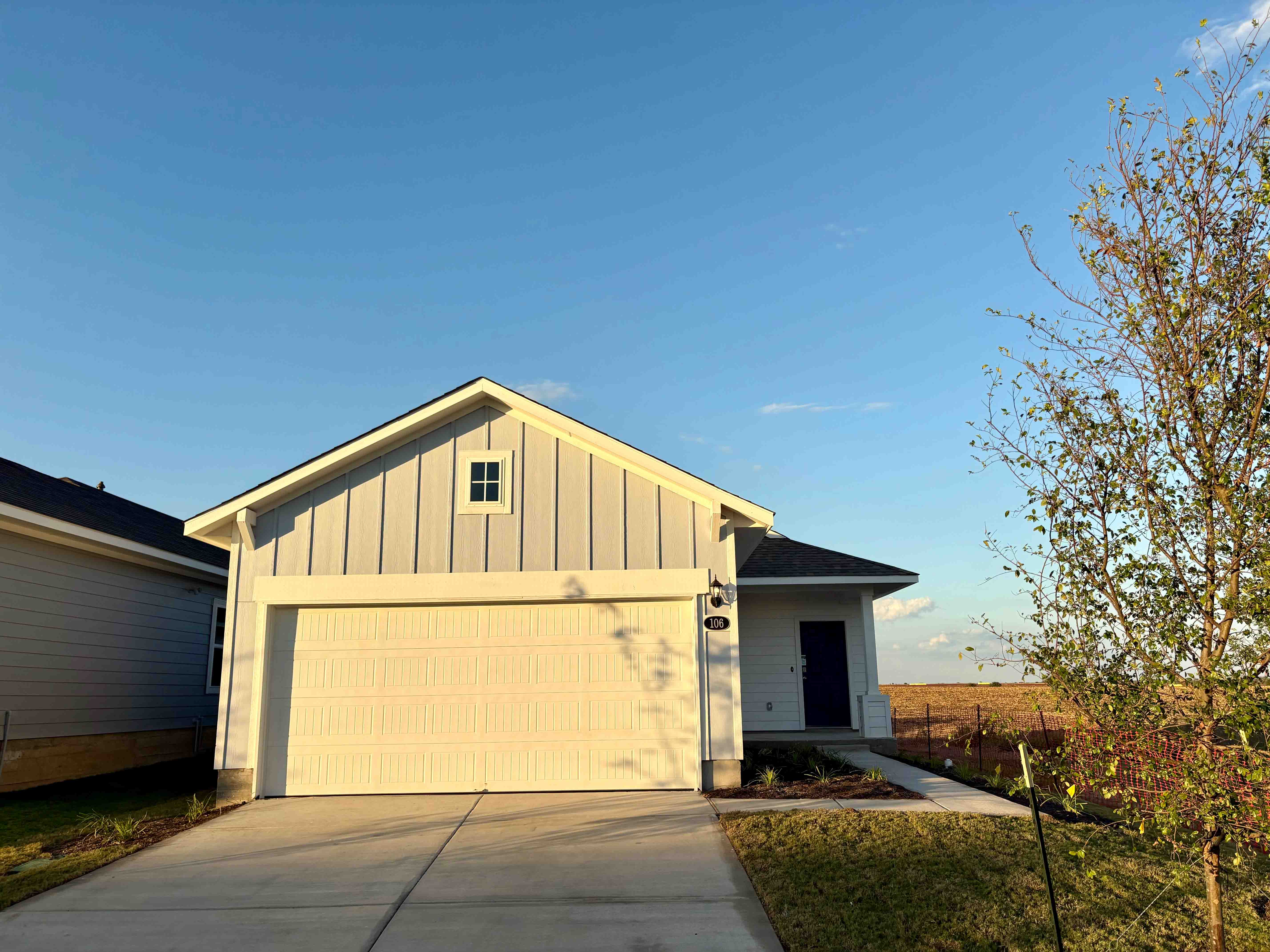 Image of a front of blue single-story home with white garage and driveway with a dirt landscape. and blue sky in the background.