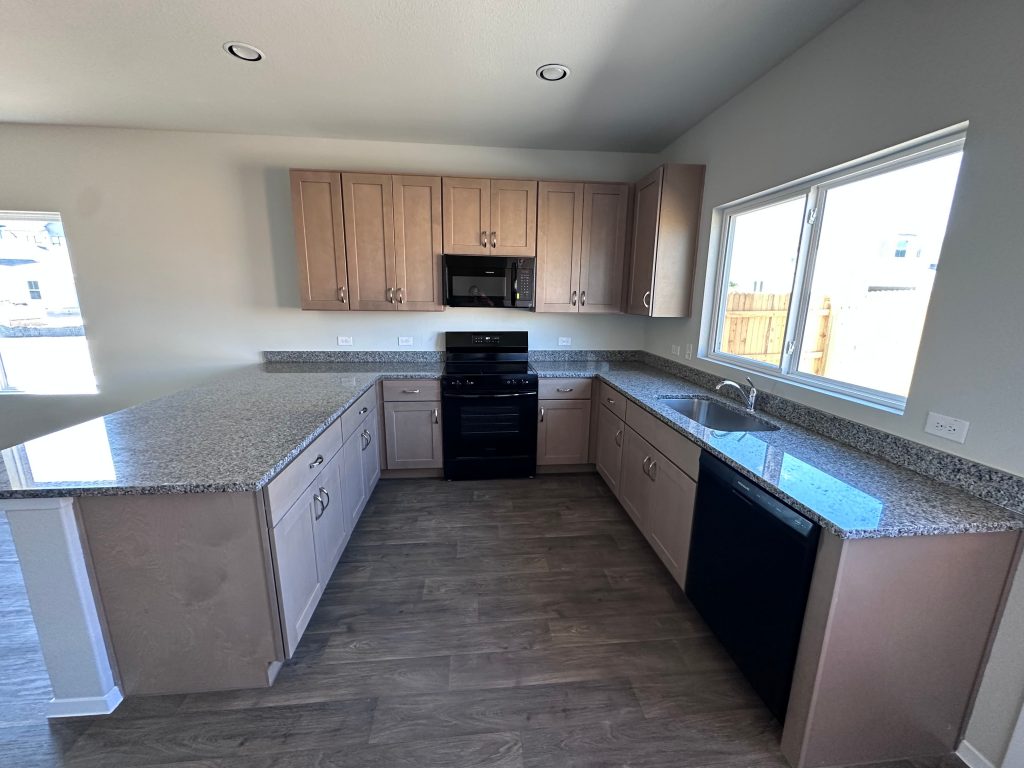 An image of a kitchen with gray and white speckled countertop, grey cabinets, black appliances.