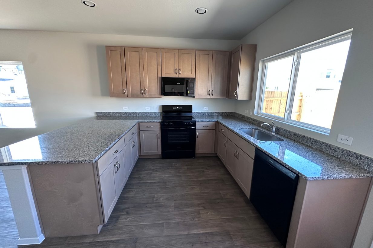 An image of a kitchen with gray and white speckled countertop, grey cabinets, black appliances.