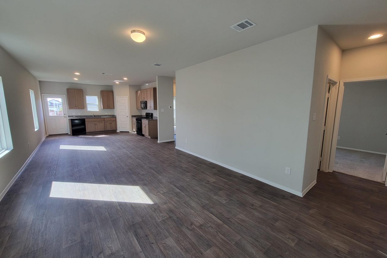 Image of home living areas including kitchen with light brown cabinets, wood-look floor, white walls, and light coming through windows