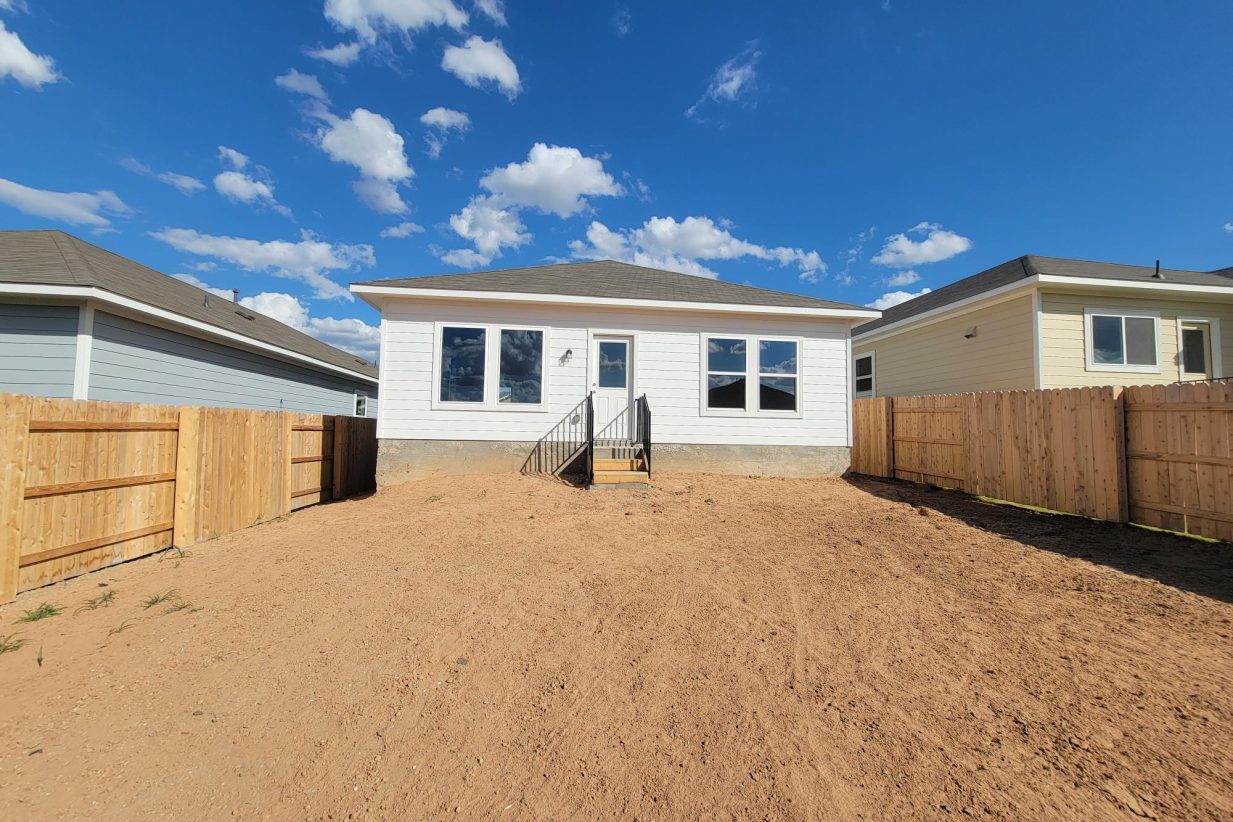 Image of rear of one story home with landscaping dirt, wood fence, and sky
