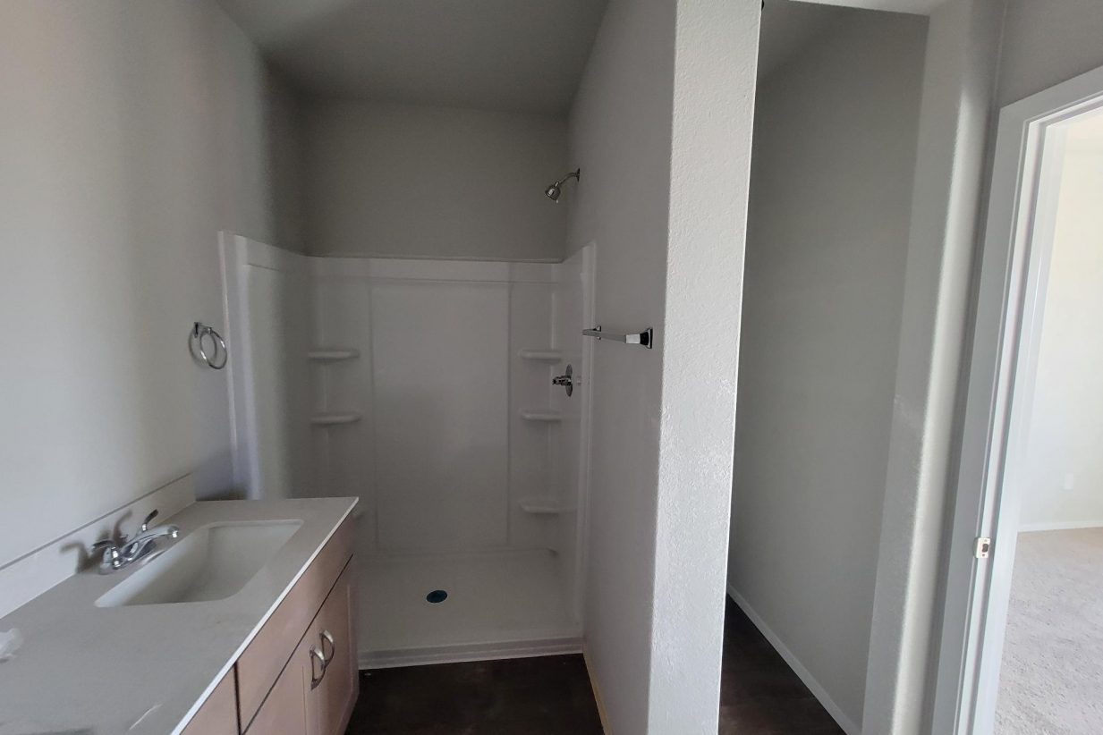 Image of home bathroom under construction with vanity with white countertop and light brown cabinet and walk-in shower