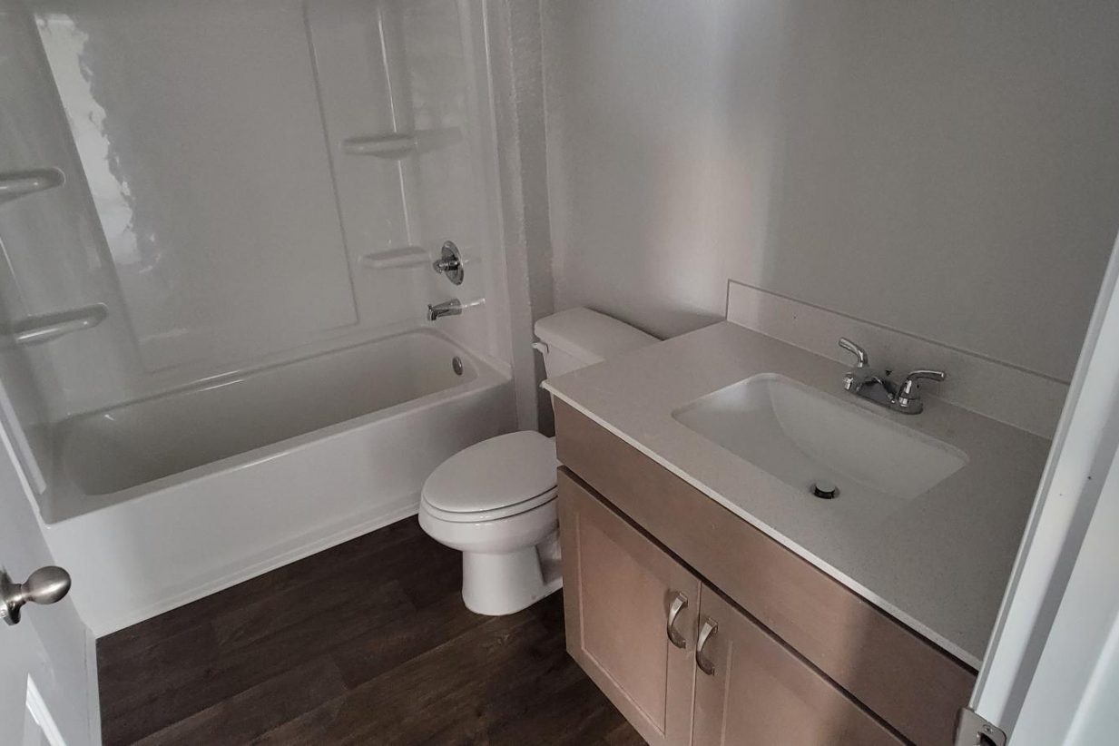 Image of home bathroom with vanity with white countertop and light brown cabinets, toilet, and tub