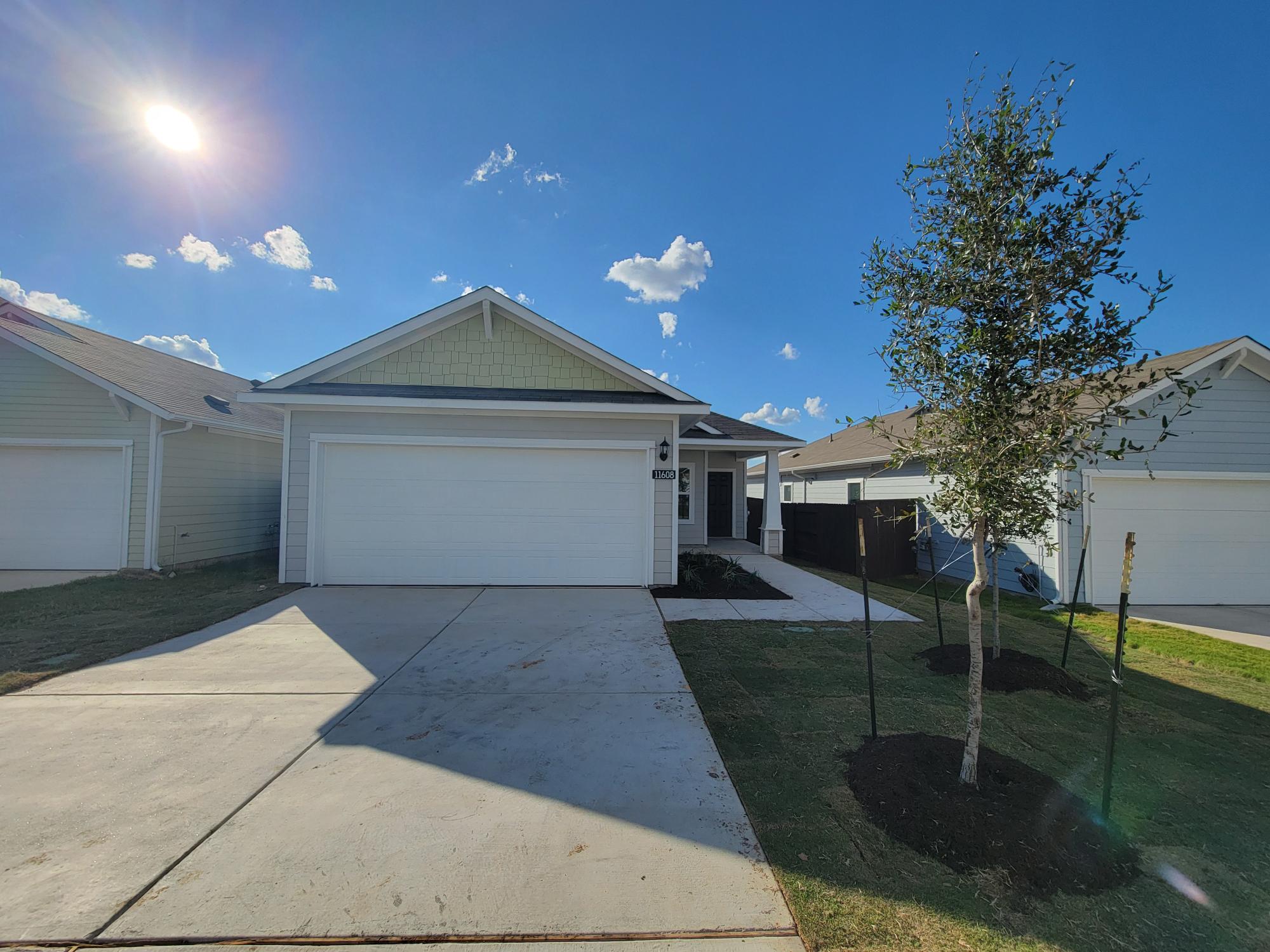Image of one story yellow home with white garage, tree, grass, and sky