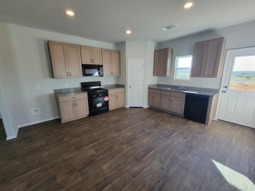 Image of home kitchen with light brown cabinets, wood-look vinyl, window over sink, and white walls
