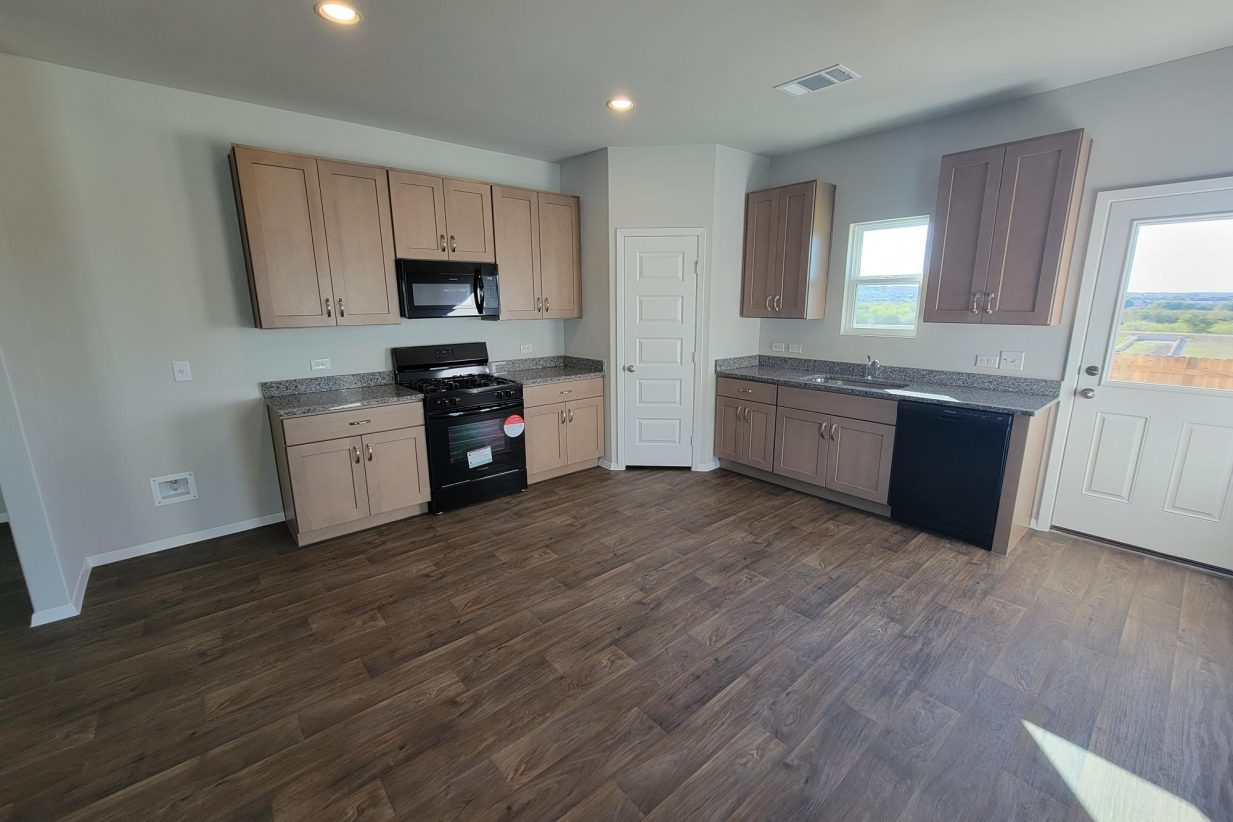 Image of home kitchen with light brown cabinets, wood-look vinyl, window over sink, and white walls