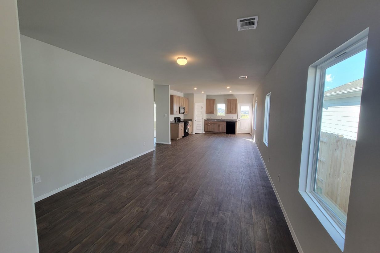 Image of home living area and kitchen with wood look floor, white walls, and windows