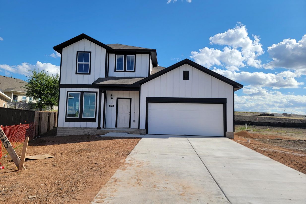 Image of two story white and black home with driveway, dirt, and sky