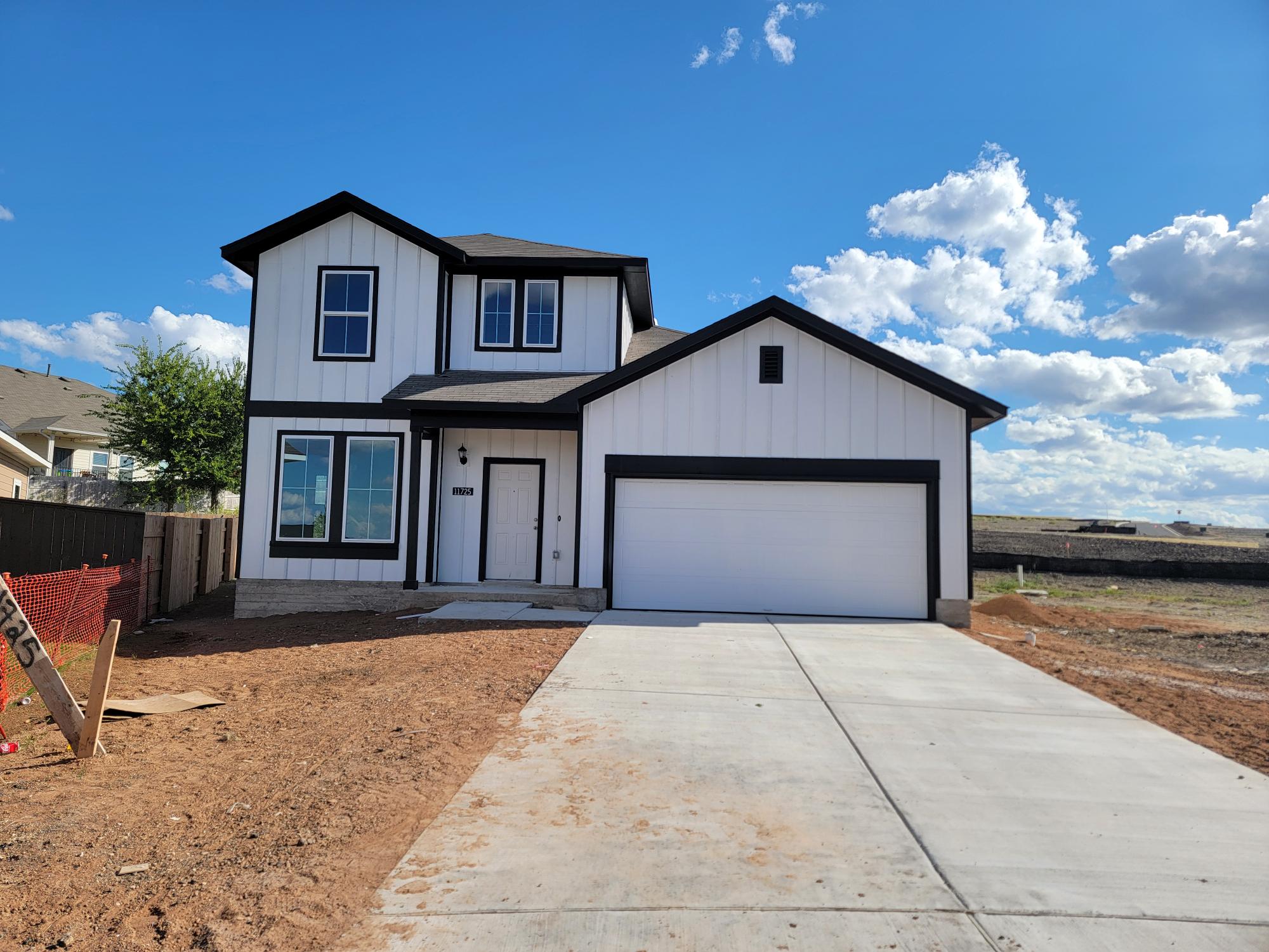 Image of two story white and black home with driveway, dirt, and sky