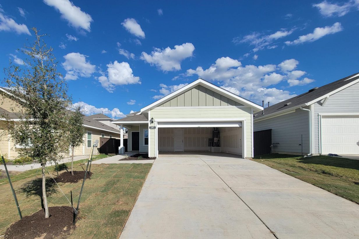 Image of one story home with driveway, tree, grass, and sky