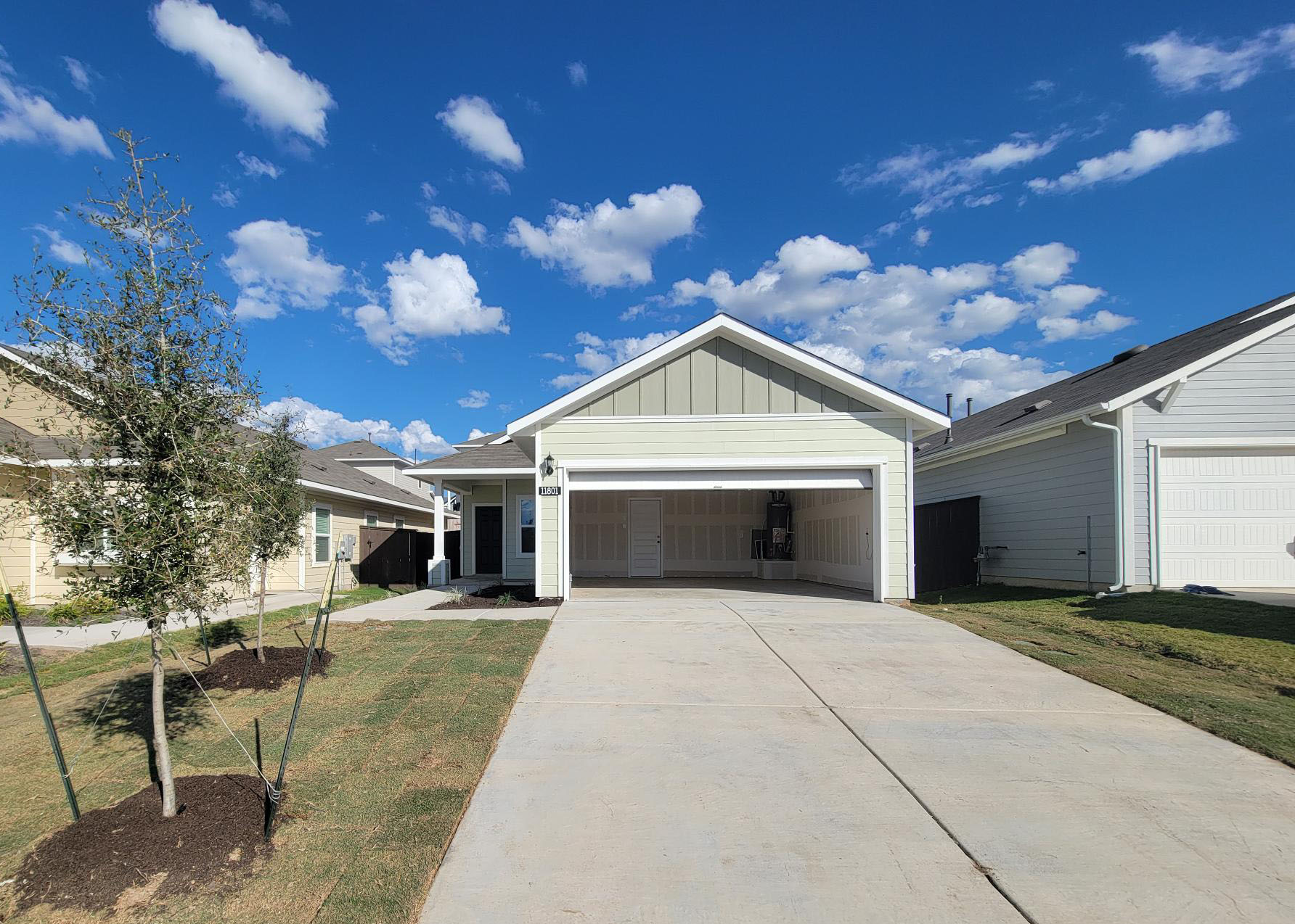 Image of one story home with driveway, tree, grass, and sky