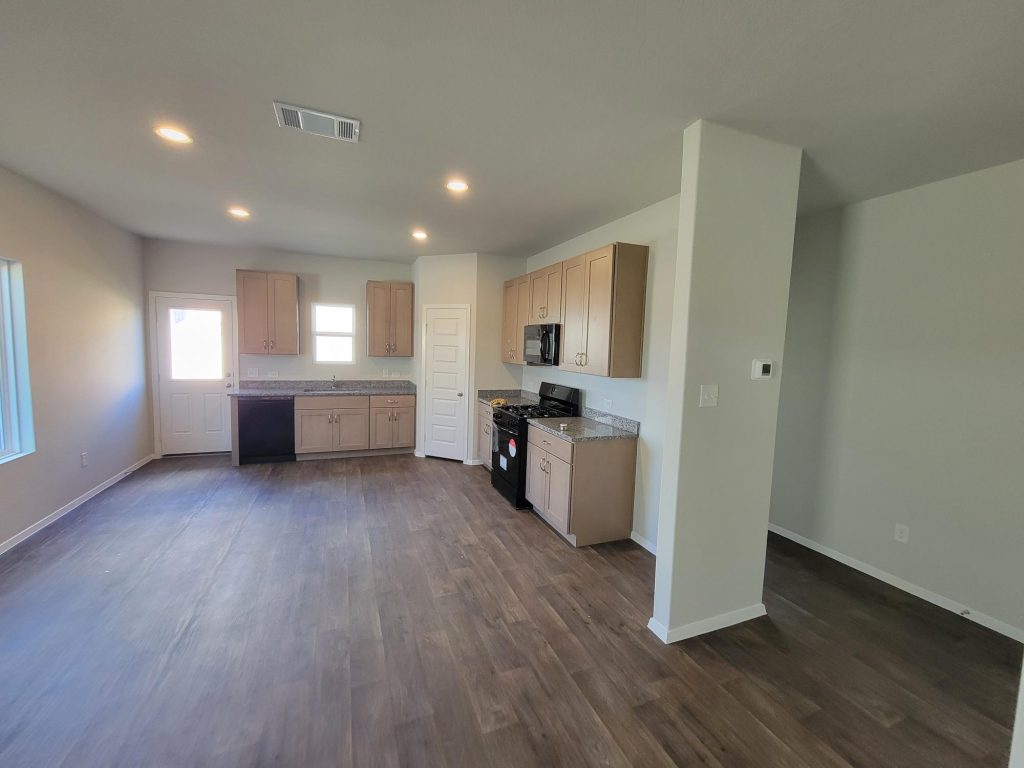 Image of home kitchen with light brown cabinets and black appliances, wood-look floor, white walls, and windows