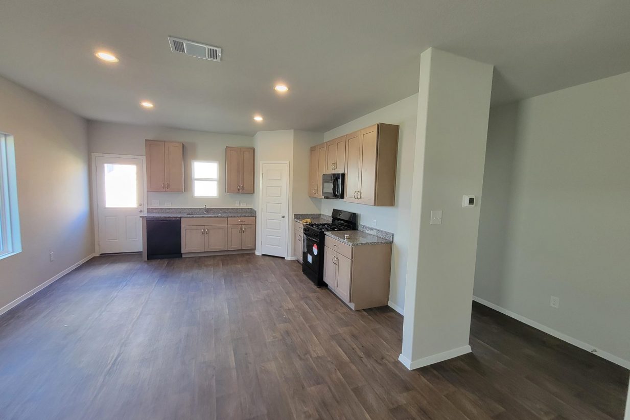 Image of home kitchen with light brown cabinets and black appliances, wood-look floor, white walls, and windows