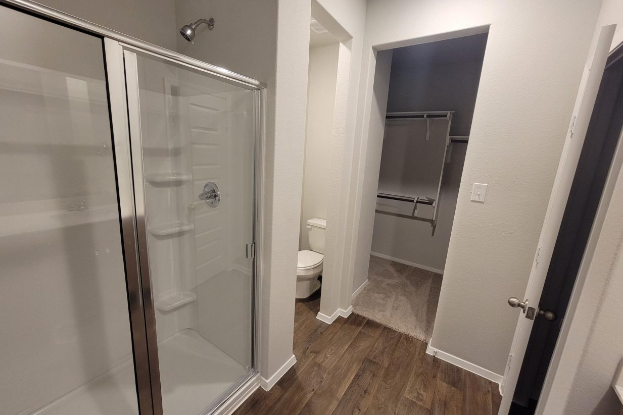 Image of home bathroom with walk-in shower, doorway to walk-in closet, wood-look floor, and white walls