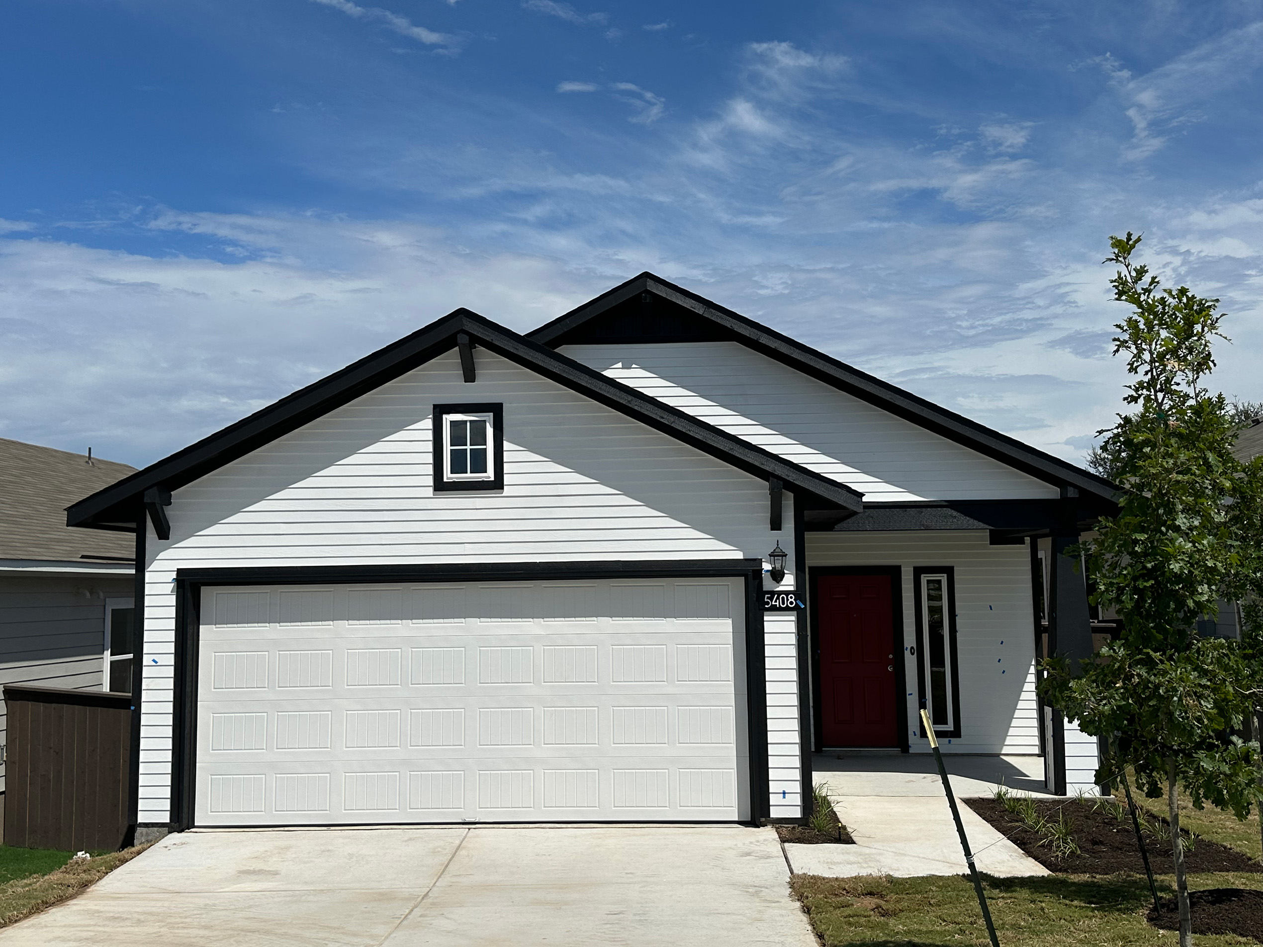 Image of one story white and black home with white garage and red front door