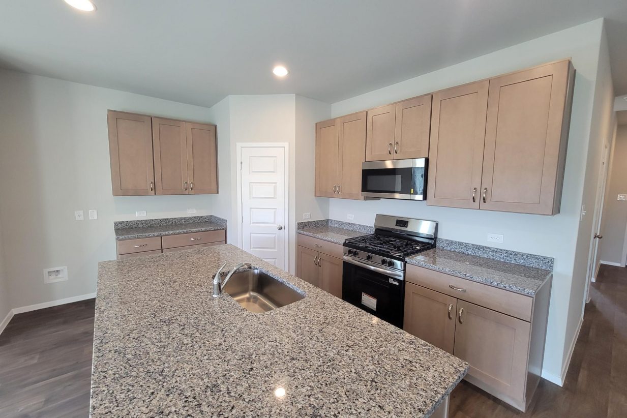 Image of home kitchen with light brown cabinets, stainless steel appliances, and center island with white walls