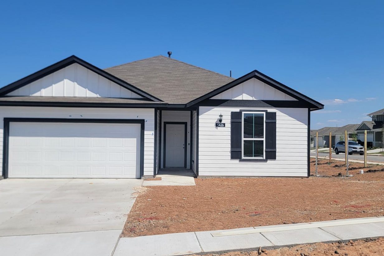 Image of one story white and black home front exterior with driveway, landscape dirt, and sky