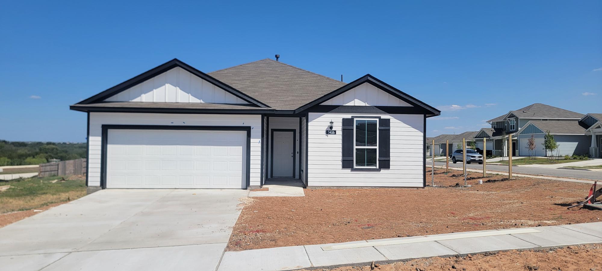 Image of one story white and black home front exterior with driveway, landscape dirt, and sky