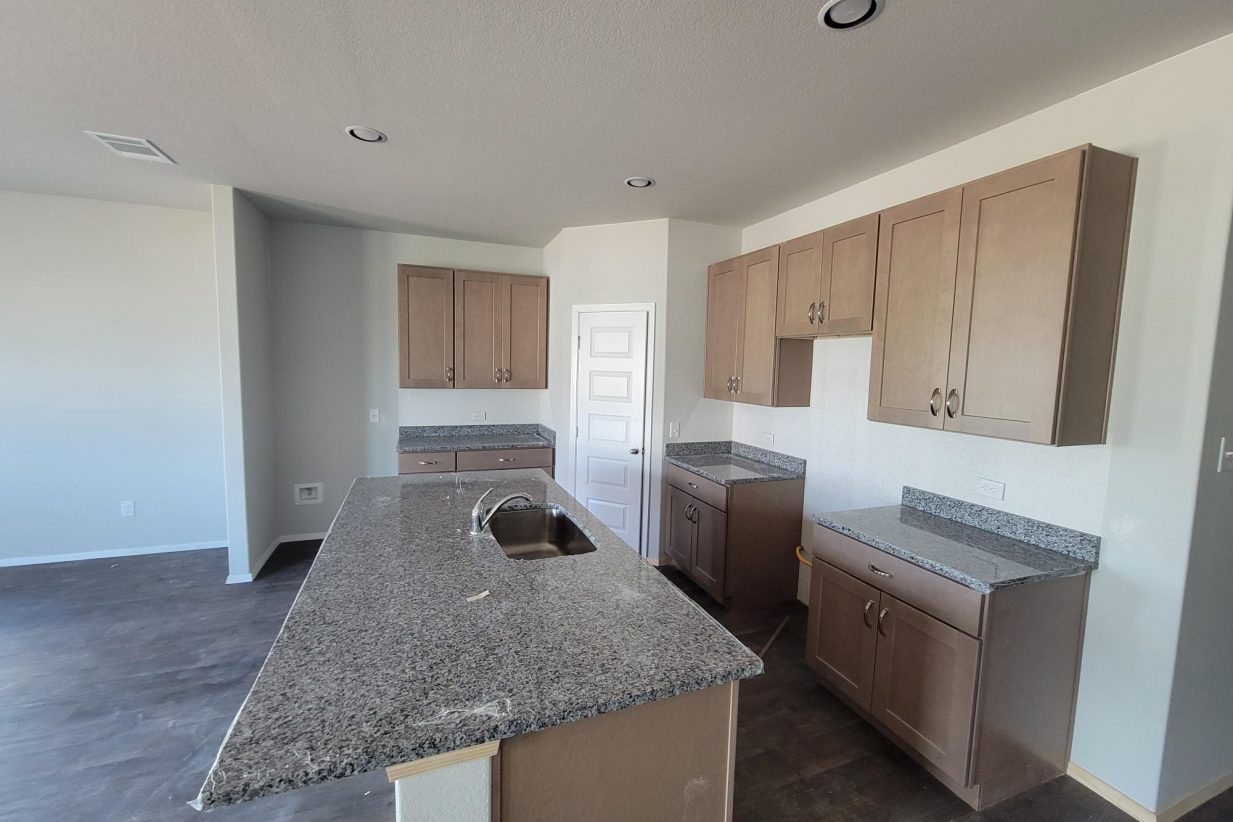 Image of home kitchen with center island, light brown cabinets, white walls, and wood look floor