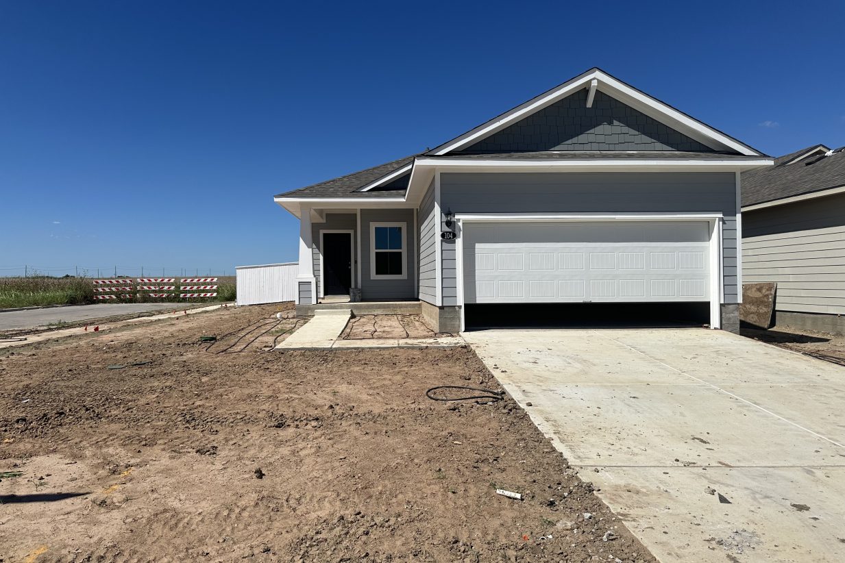 Image of exterior of one story blue home of a corner lot without grass
