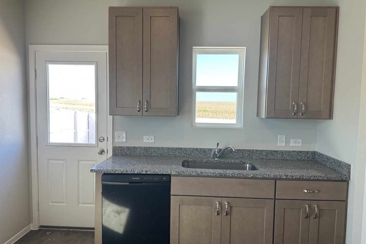 Image of kitchen with rear door, window over kitchen sink, and light brown cabinets