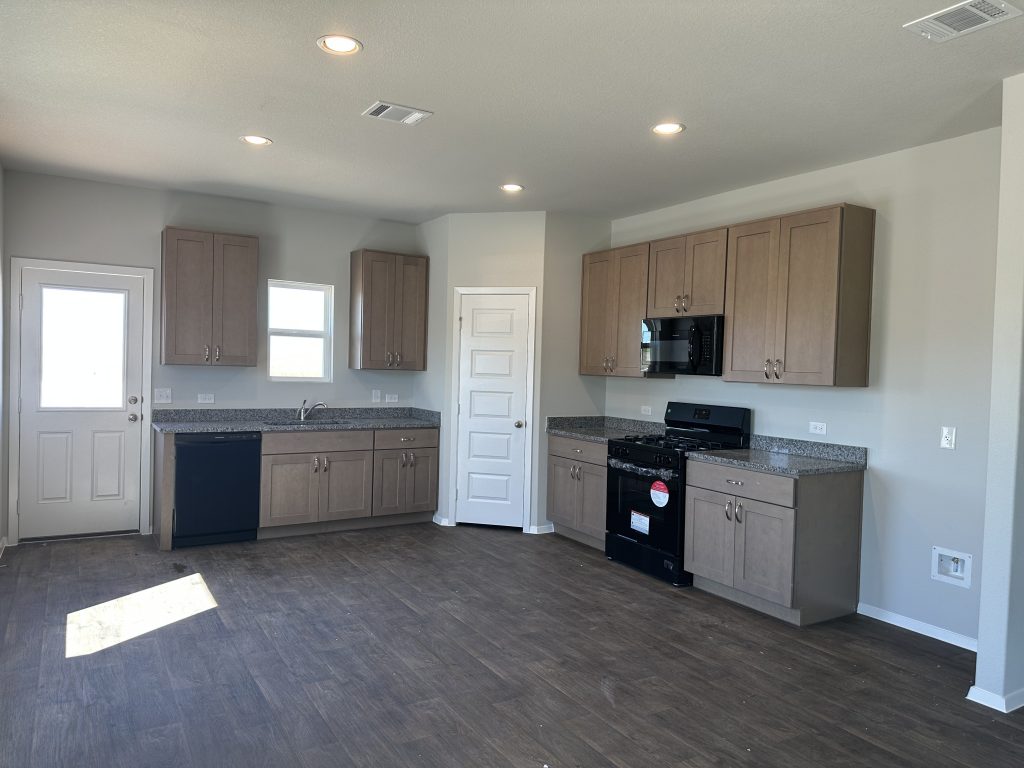 Image of kitchen with wood-look vinyl floor, light brown cabinets, and black appliances