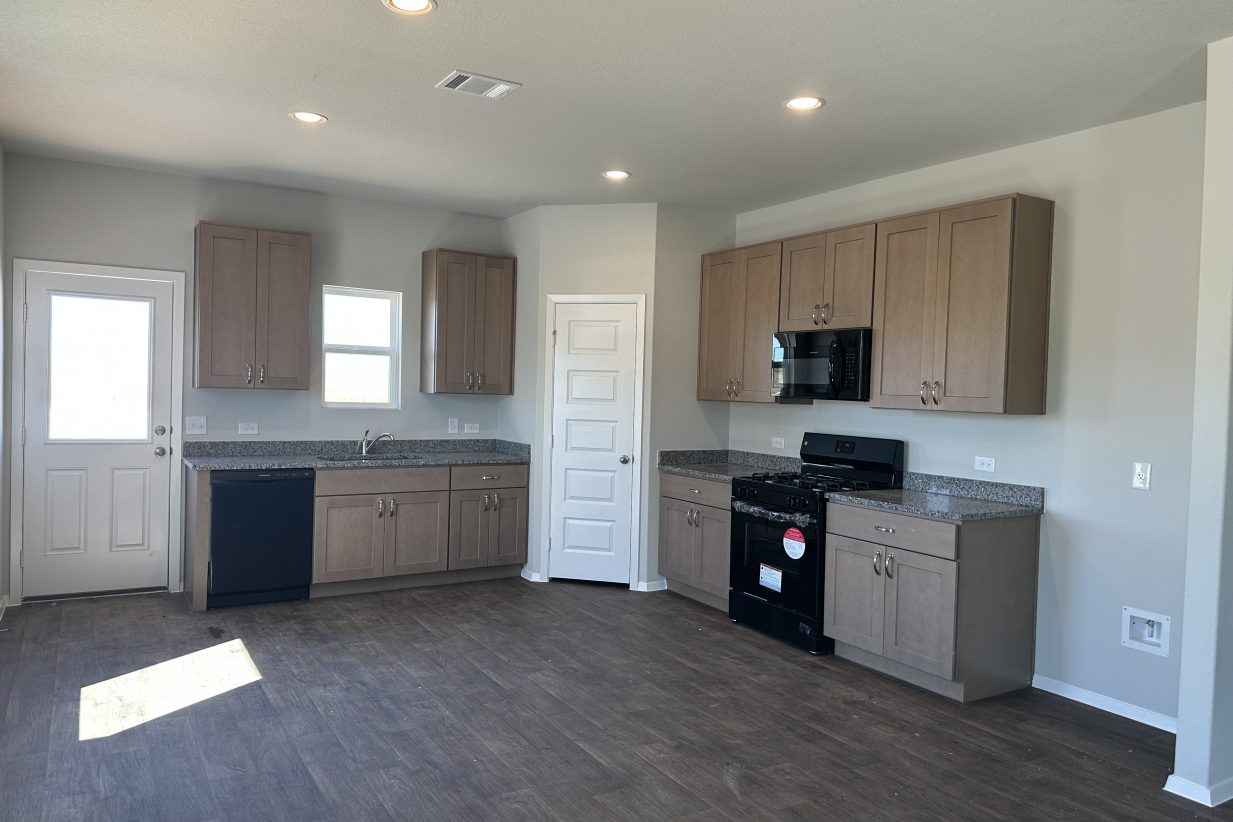 Image of kitchen with wood-look vinyl floor, light brown cabinets, and black appliances
