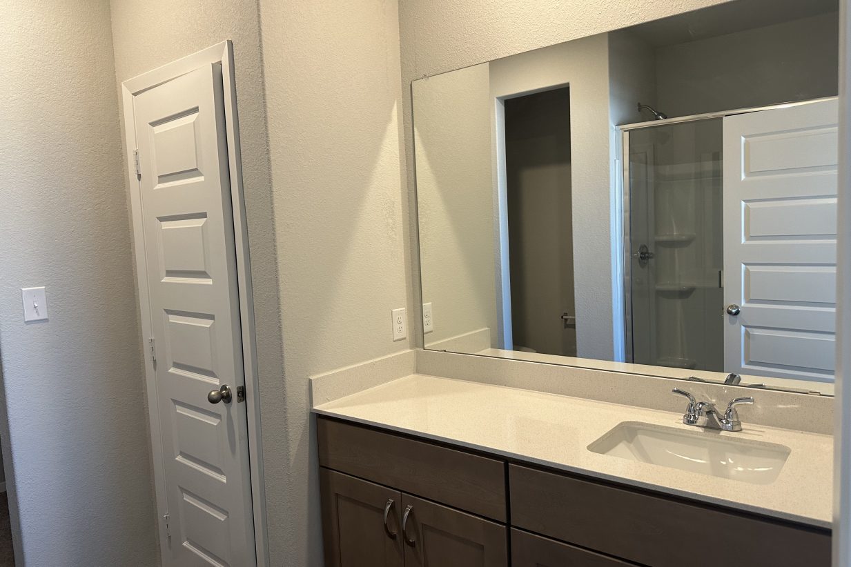 Image of bathroom with vanity with white countertop, light brown cabinets, and reflection of shower and water closet