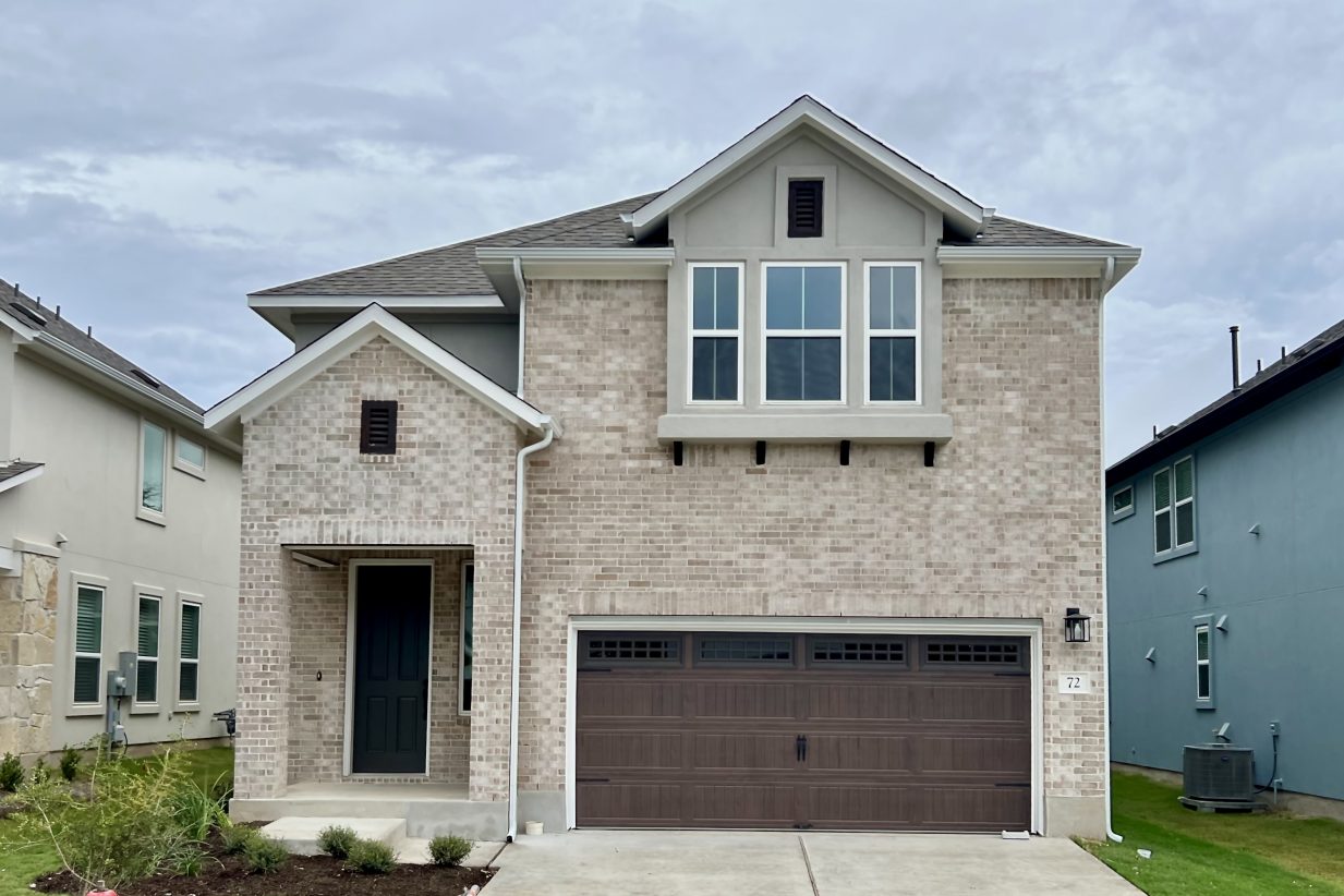 Front exterior of two-story brick house with a brown garage door and a green landscape.