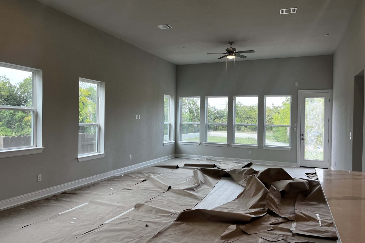 A room under construction with white framed windows, white framed base boards, and grey painted wall.